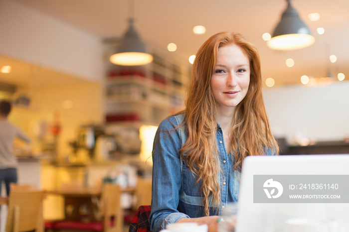 Portrait smiling young woman working at laptop in cafe