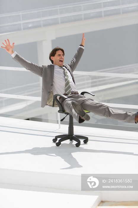 Playful businessman rolling down ramp in office chair