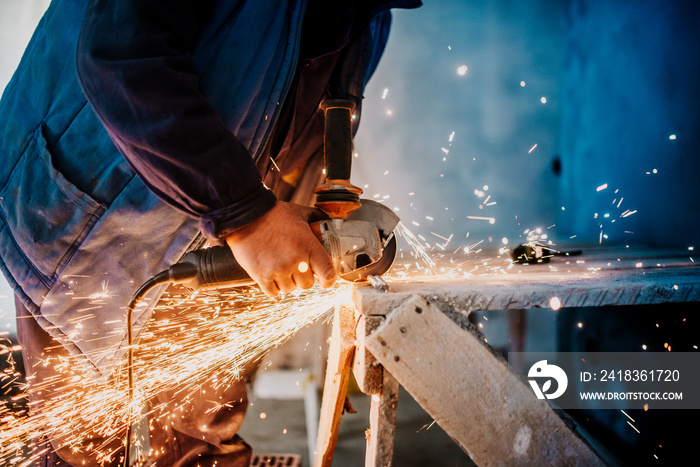 Metalworker cutting iron and metal with a rotary angle grinder and working, generating metal sparks