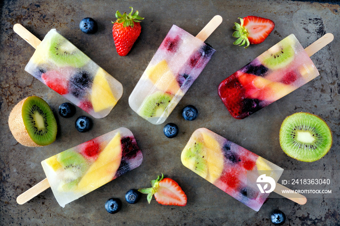 Healthy mixed fruit summer popsicles. Top view scattered on a rustic dark background.