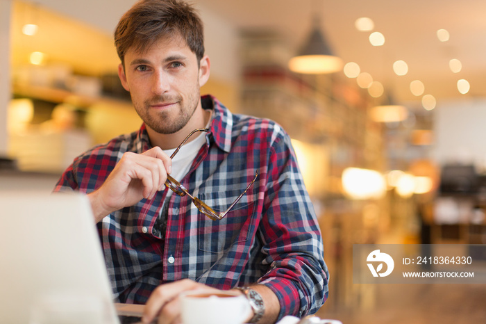 Portrait confident man working at laptop in cafe