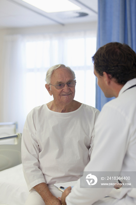 Smiling male senior patient talking with doctor in hospital room