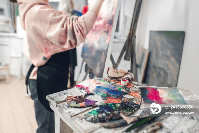 Palette with oil paints on the background of a female artist painted on canvas. An abstract photo of