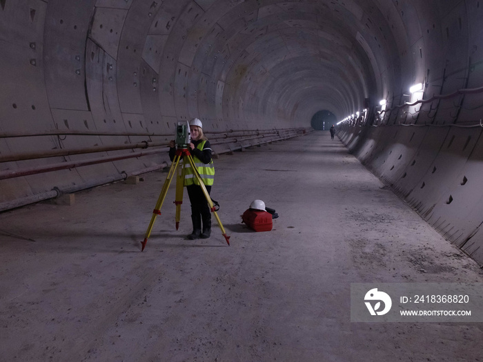 Pretty young mining surveyor woman works on the geodetic total station in the tunnell of metro under