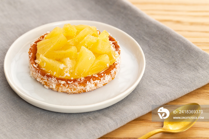 Small pineapple tart or tartlet with glazed pineapple fruit pieces and grated coconut on grey napkin