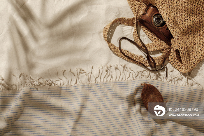 Striped linen beach towel with fringes, woven bag, vintage camera and coconut on sandy beach with sh