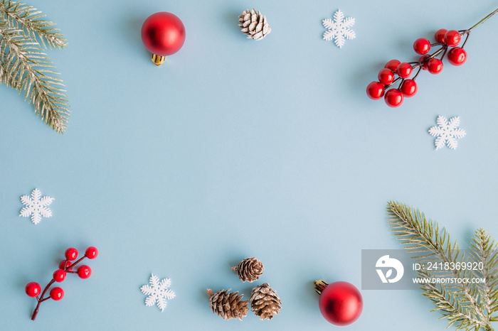 Christmas frame made of fir branches, red berries, snowflakes, bauble decoration and pine cones on b