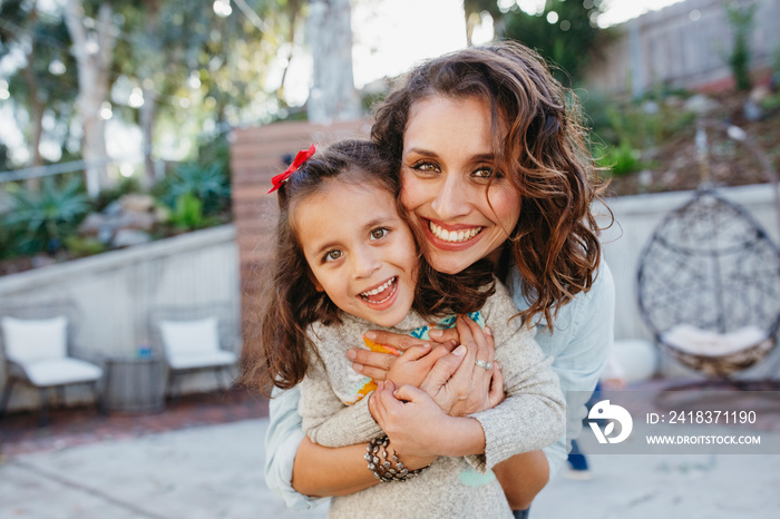 Portrait of happy mother embracing cute daughter while standing in yard