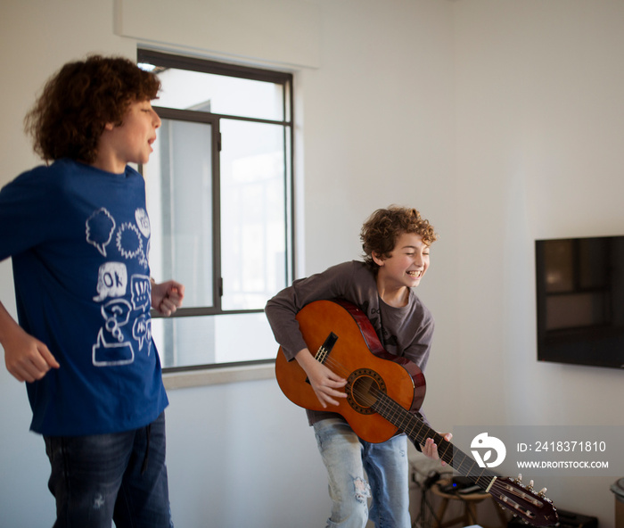 Mother playing guitar while sons dancing against wall in bedroom at home