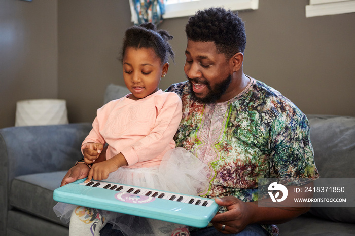 Girl on sofa with father playing toy keyboard