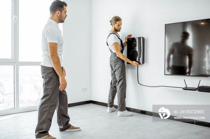 Two professional workmen in workwear installing luxury audio system in the white living room. Home a