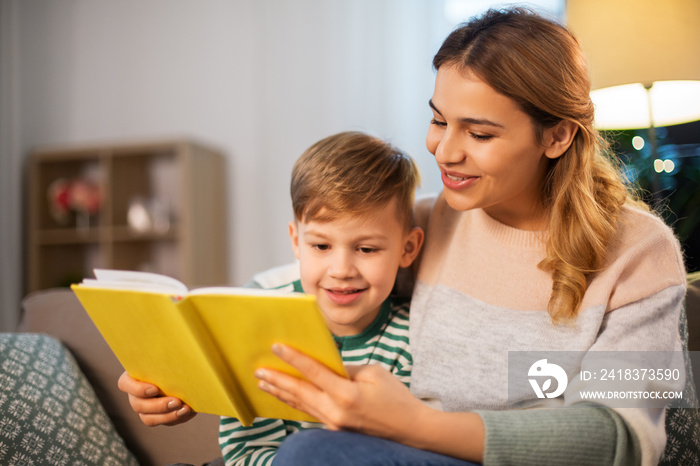 family, leisure and people concept - happy smiling mother and little son reading book sitting on sof