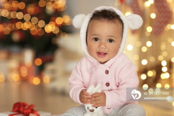 Cute little baby with toy against blurred Christmas lights