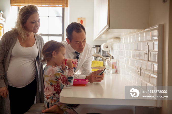 Father showing mobile phone to family in kitchen at home