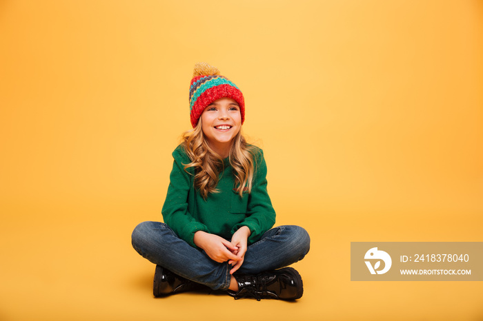 Happy Young girl in sweater and hat sitting on floor