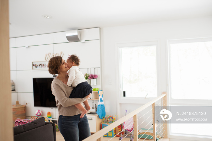 Happy mother carrying cute daughter while standing against wall at home