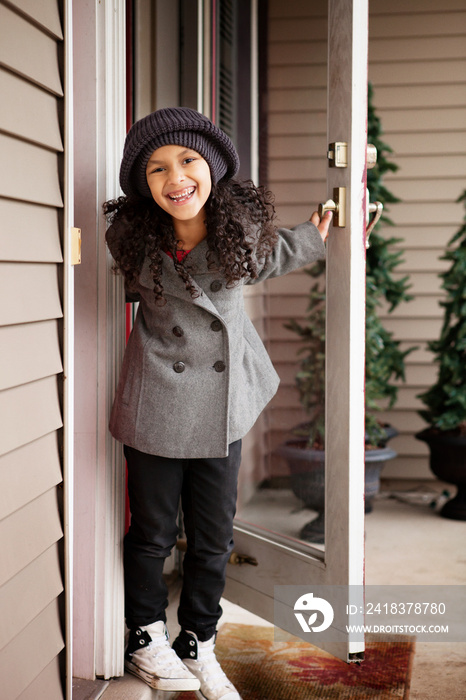 Smiling girl holding house door ajar