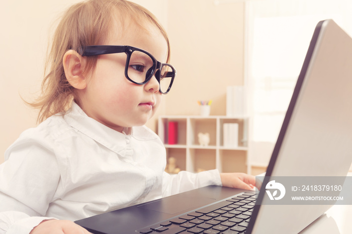 Smart toddler girl wearing big glasses using her laptop