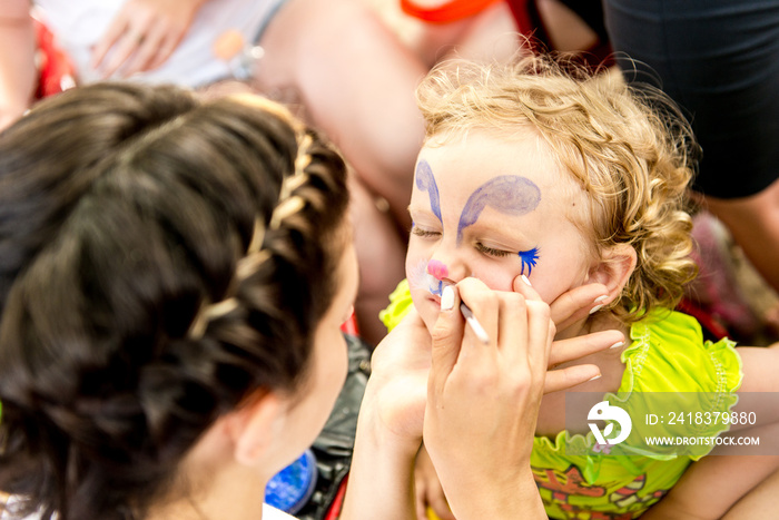 woman painting face of kid outdoors