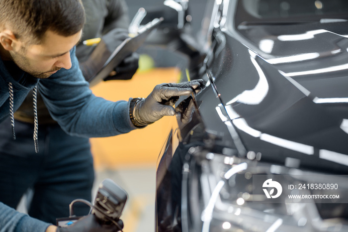 Car service worker examining vehicle body for scratches and damages, taking a car for professional a