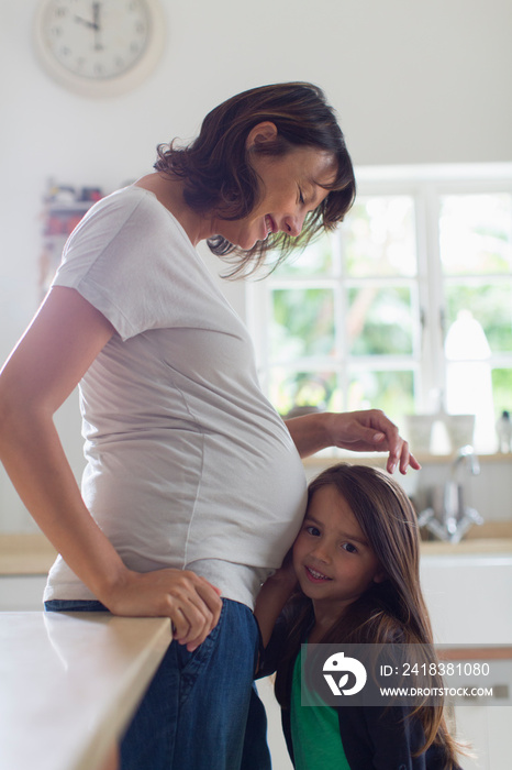 Curious daughter listening to stomach of pregnant mother