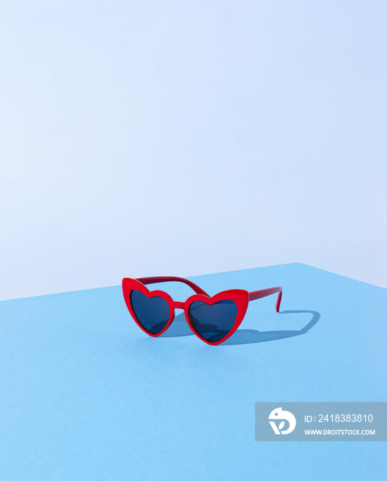 由红色心形太阳镜和蓝色粉彩背景下的阳光阴影制成的创意