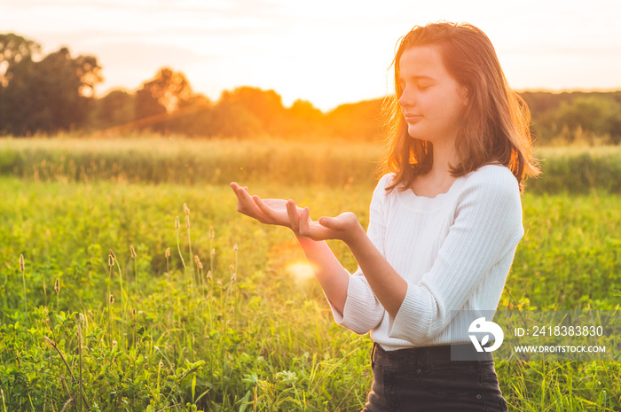 Teenager Girl closed her eyes, praying in a field during beautiful sunset. Hands folded in prayer co