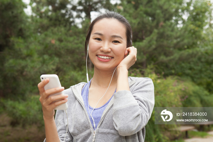 Portrait of young female runner selecting music from smartphone in park