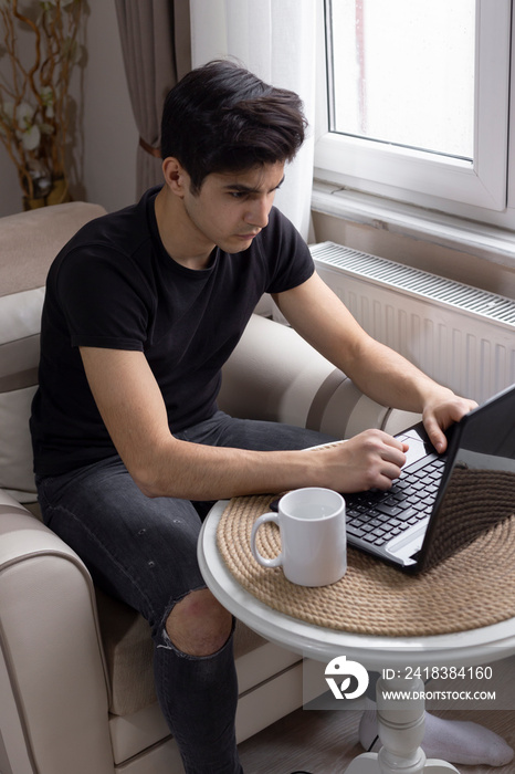 Teenage male student is studying at home, listening to music and surfing the internet.