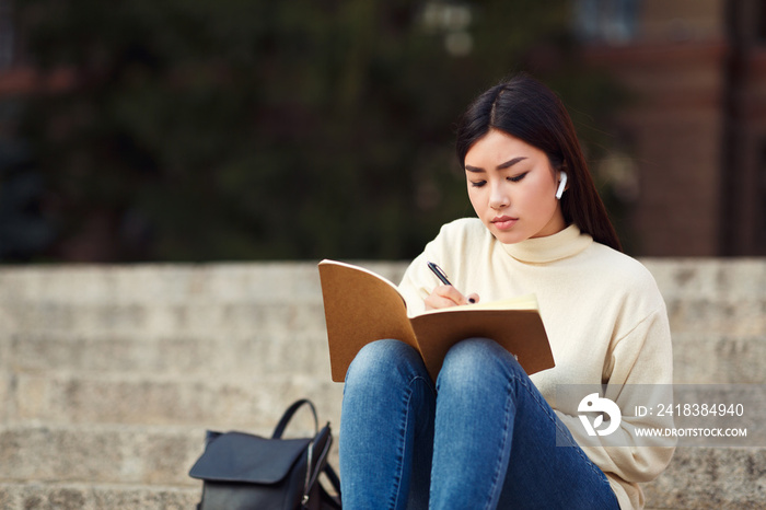 Girl in airpods writing in diary, preparing for lecture