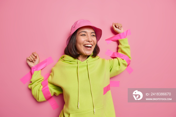 积极的亚洲女人笑得很开心，用胶带粘在墙上，穿着巴拿马风和连帽衫