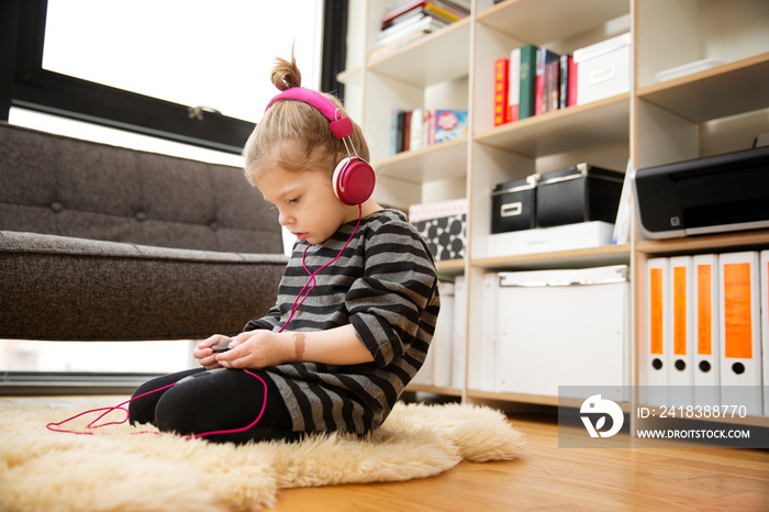 Girl (4-5) sitting on rug listening to music