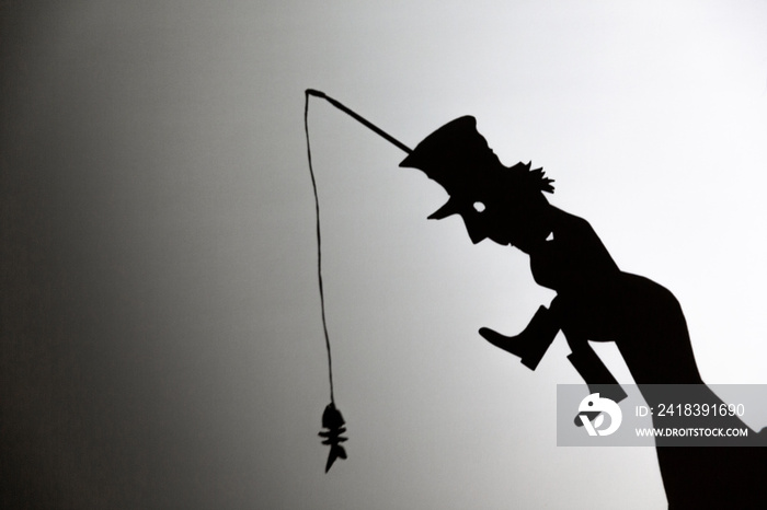 play shadow projected against a white background. a homeless man with a rod fishing