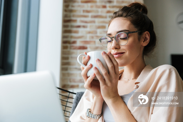 Image of woman working with laptop and drinking coffee while sitting