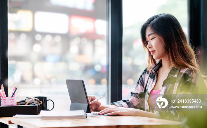 Young beautiful asian woman using tablet working online while sitting at cafe.