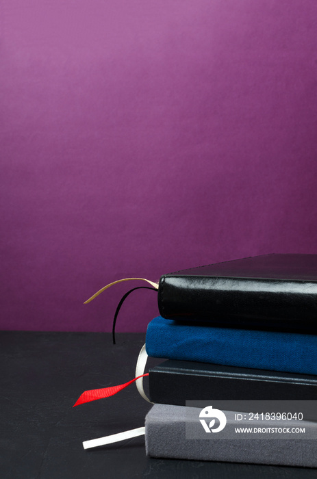 Vertical image.Stack of blue and dark notebooks on the dark desk against purple background.Empty spa