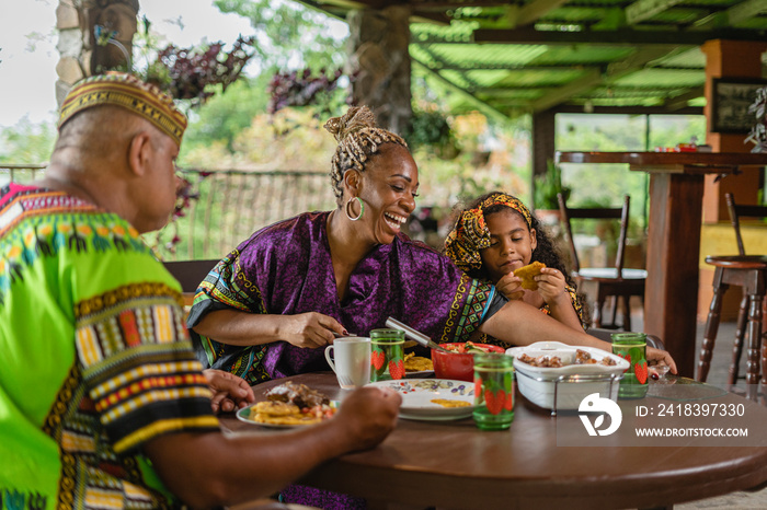 Imagen horizontal de una familia afrocaribeña muy alegre sentados  juntos a la mesa degustando un de