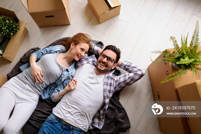 Beautiful young couple lying on the floor among cardboard boxes in their new apartment they just mov