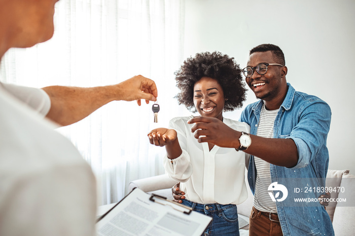 Real estate agent giving keys to couple of customers. Happy young couple getting keys of their new h