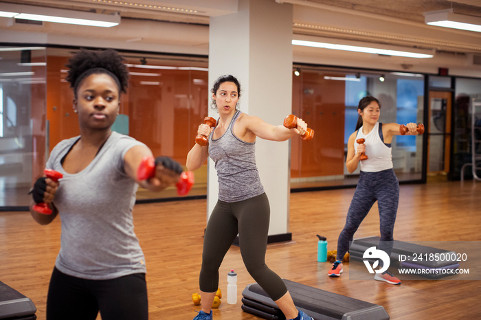 Confident female athletes exercising with dumbbells while standing on hardwood floor in gym