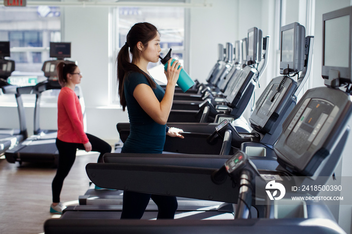 Side view of woman drinking water while exercising on treadmill in gym