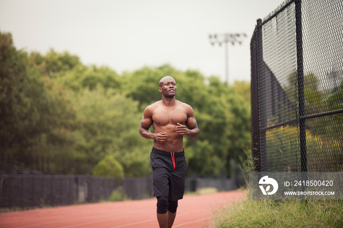 Shirtless male athlete running on sports track against trees