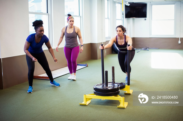 Trainers looking at female athlete pushing weight sled in gym