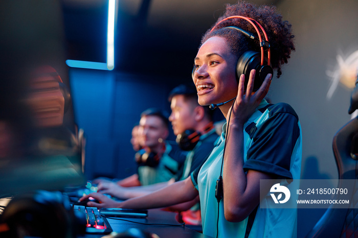 Happy African female gamer wearing headphones looking at PC screen and smile during esports tourname