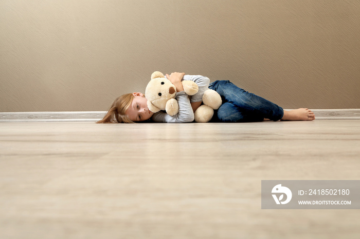 Upset girl with teddy bear lying on the floor at home