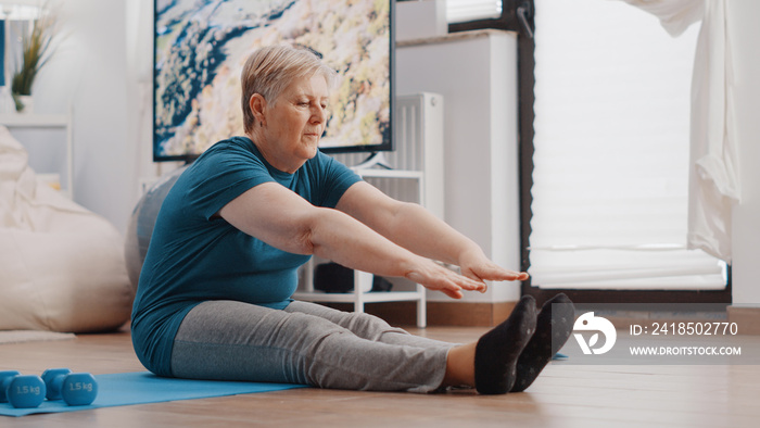 老年妇女在瑜伽垫上做伸展运动。老年人弯腰伸展胳膊和腿