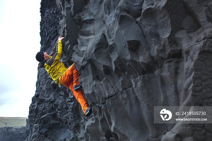 male rock climber. rock climber climbs on a rocky wall on the ocean bank. man makes hard move withou