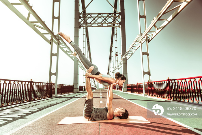 Young couple practicing acroyoga outdoors on the bridge