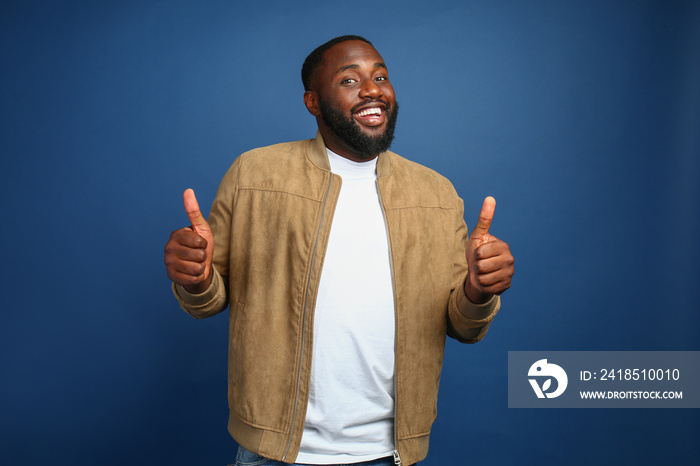 Happy African-American man showing thumb-up gesture on color background