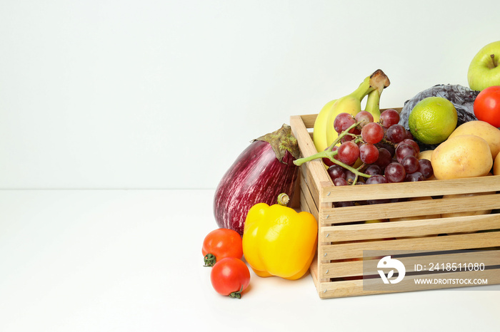 Wooden box with different vegetables and fruits on white table